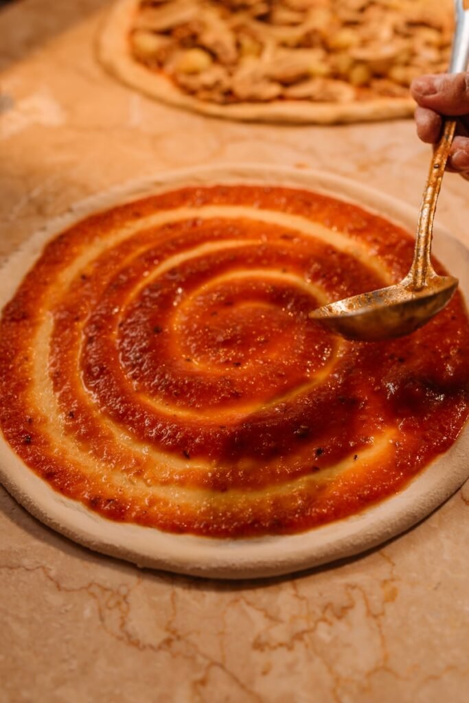 Sauce being spread on pizza dough in a spiral.