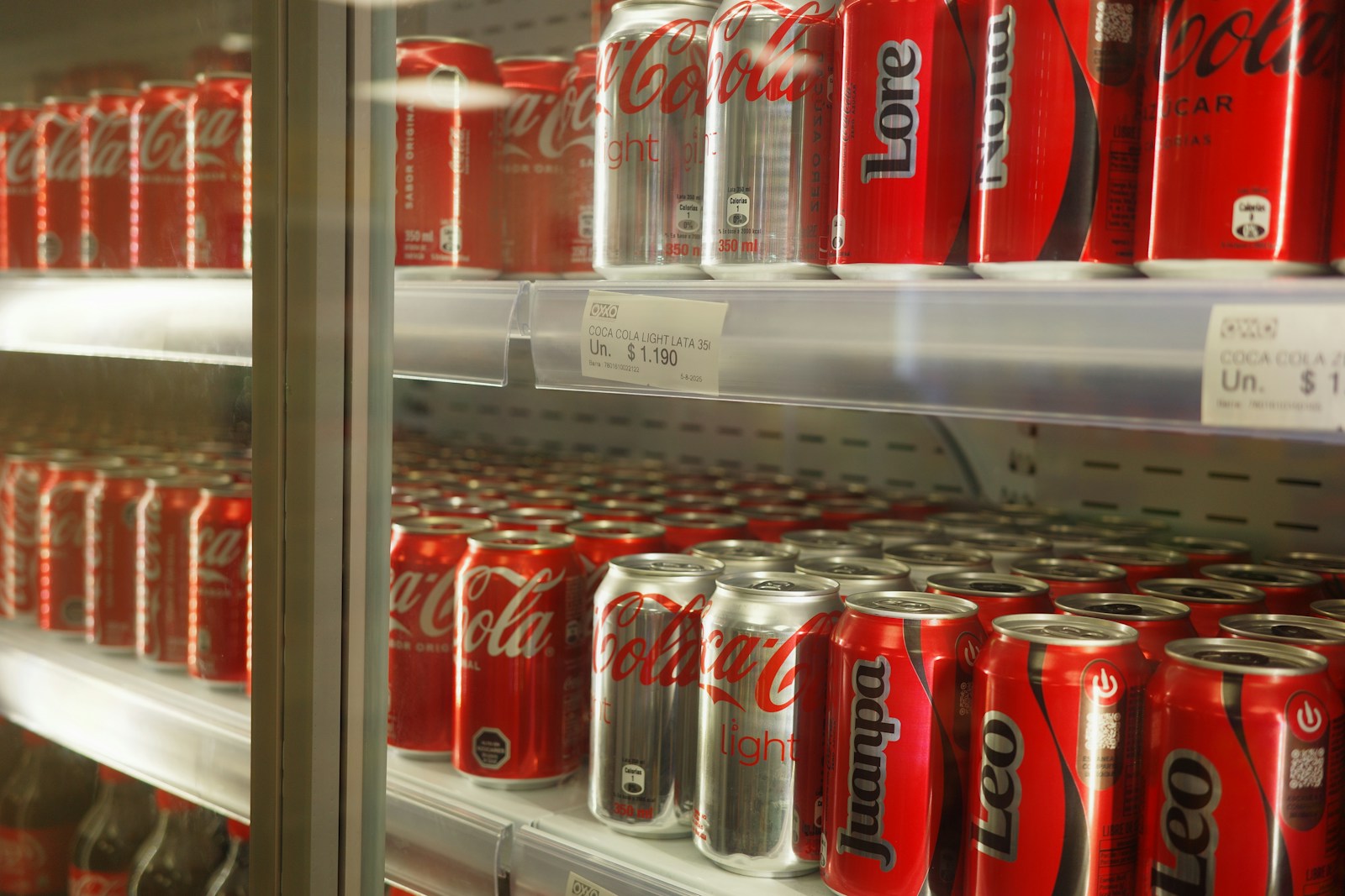 Rows of coca-cola cans stocked in a refrigerator.